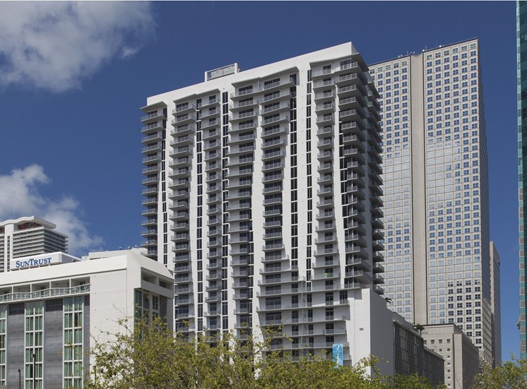 A tall white building with balconies is in the foreground of a cityscape.